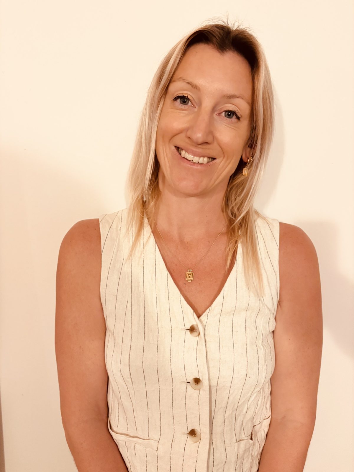 Vicki Standley, occupational therapist — a warm, head-and-shoulders portrait. Linen striped vest, soft cream wall behind.